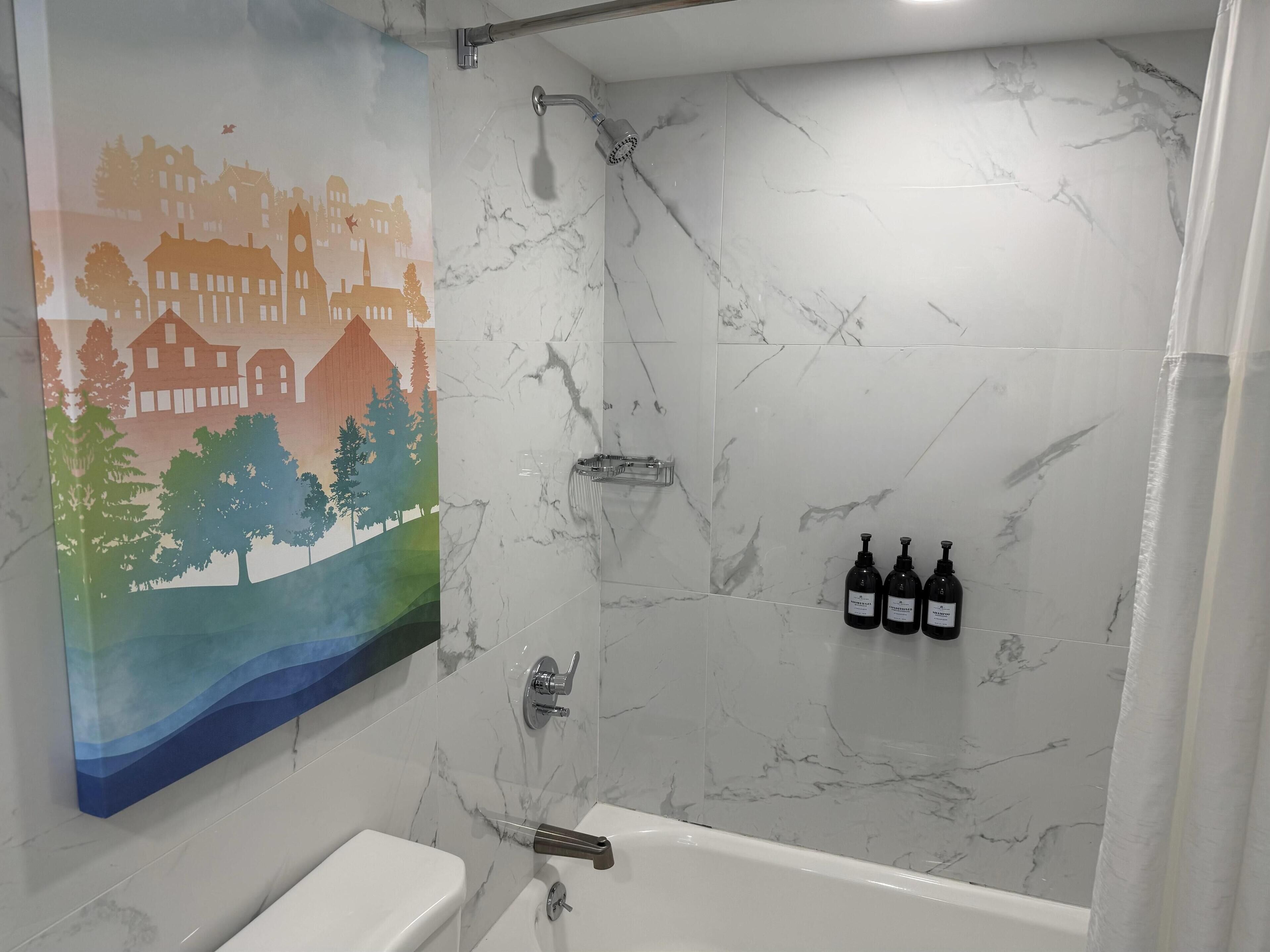 A bathroom with a marble wall, a shower, a toilet, and a painting of a landscape.
