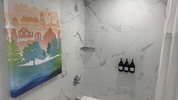A bathroom with a marble wall, a shower, a toilet, and a painting of a landscape.