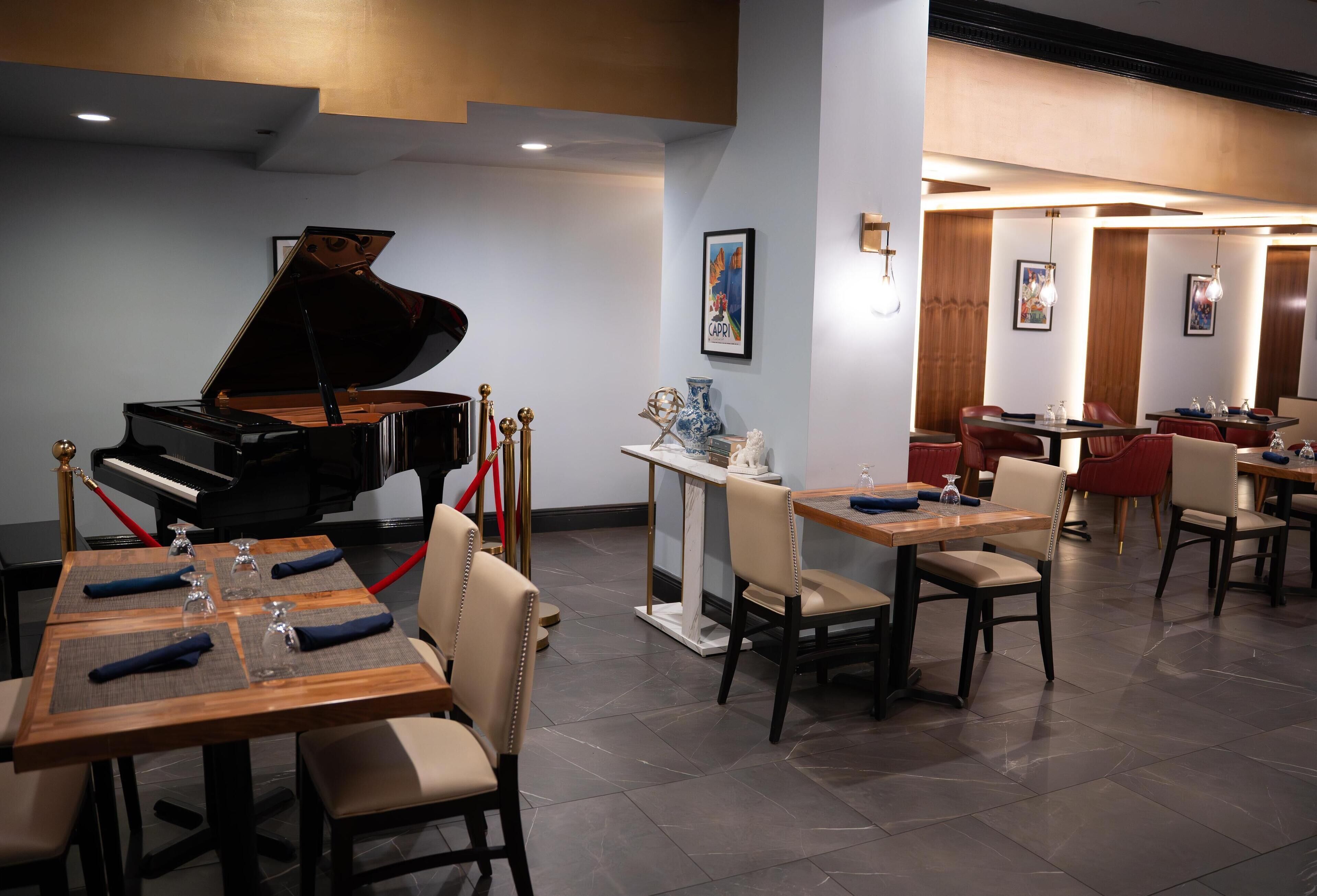 A restaurant with a grand piano, tables with chairs, and a bar area.