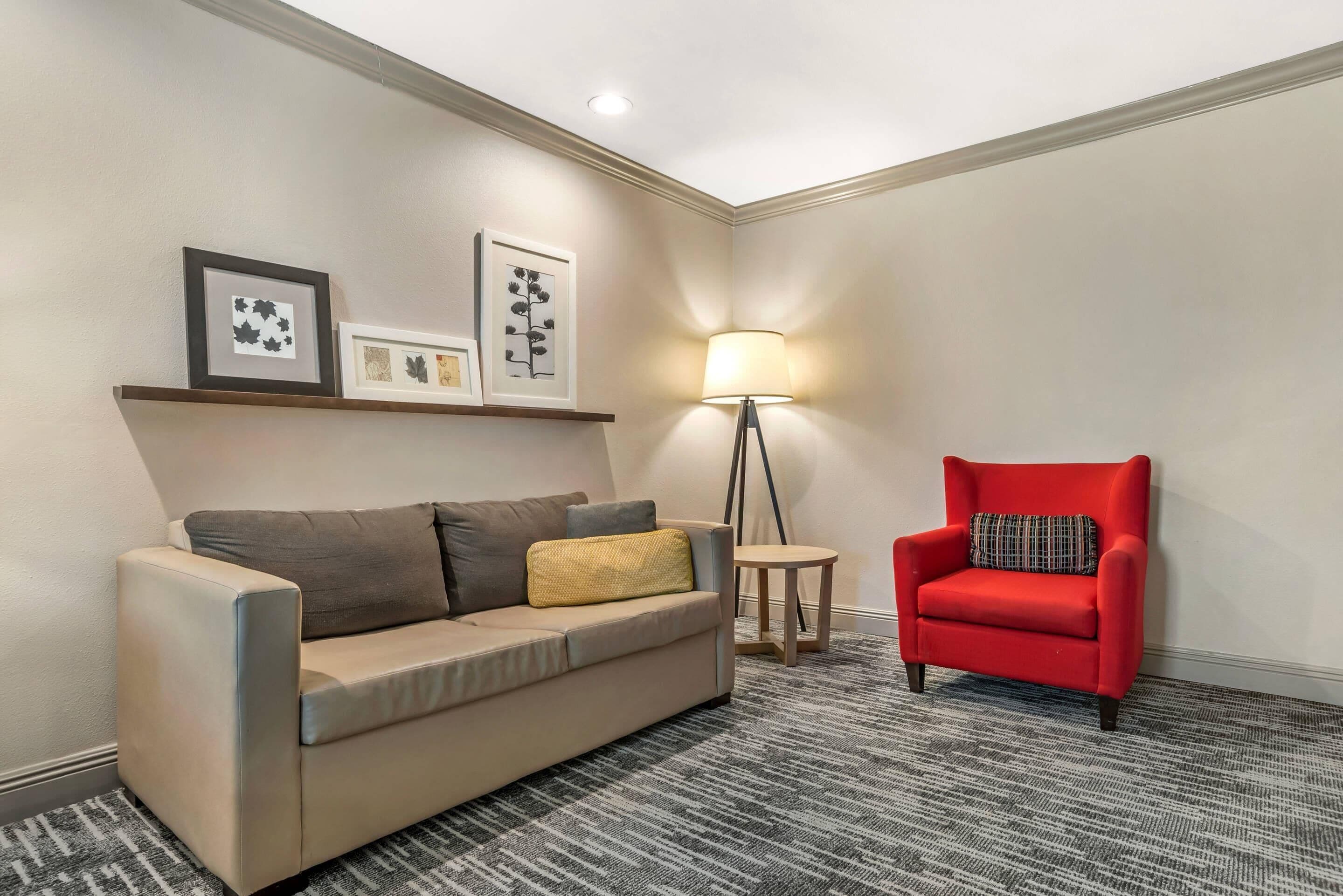 A beige sofa, a red armchair, a floor lamp, and framed artwork on the wall.