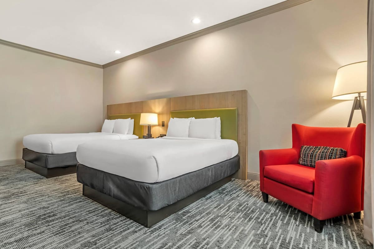 A hotel room with two beds, a red armchair, a lamp, and a patterned carpet.