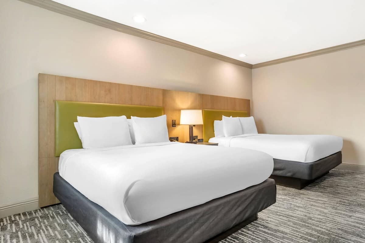 A hotel room with two beds, a headboard, bedside lamps, and a carpeted floor.