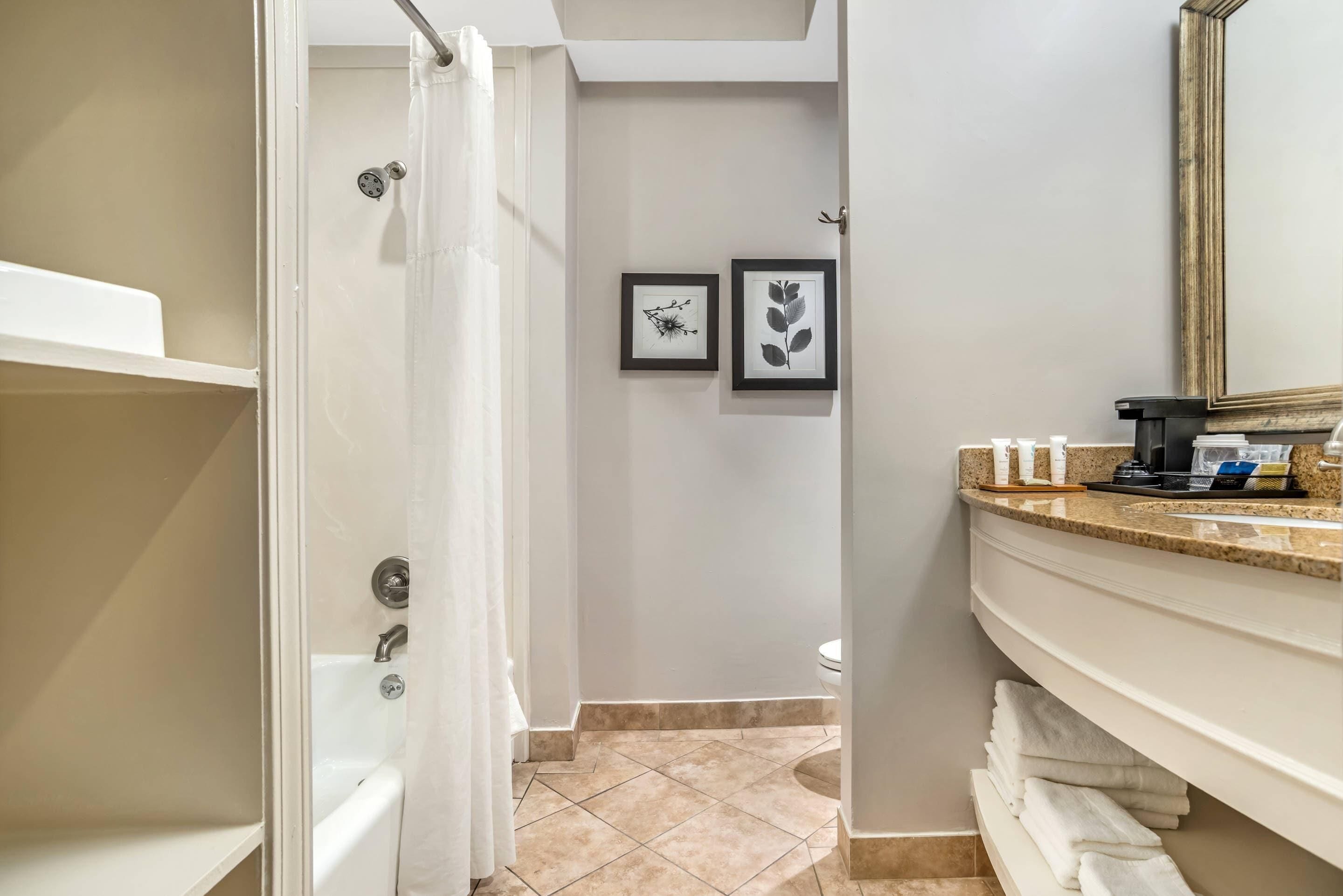 A bathroom with a shower, a toilet, and a sink with a towel rack. There are two framed pictures on the wall.