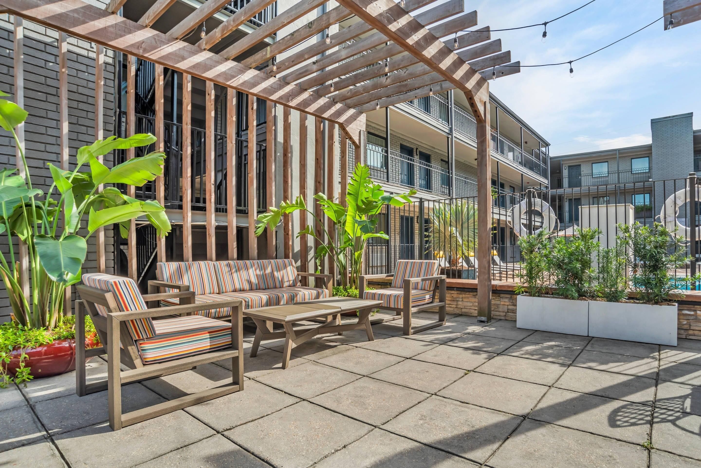 Un patio con mobiliario exterior, una pérgola y plantas en macetas.