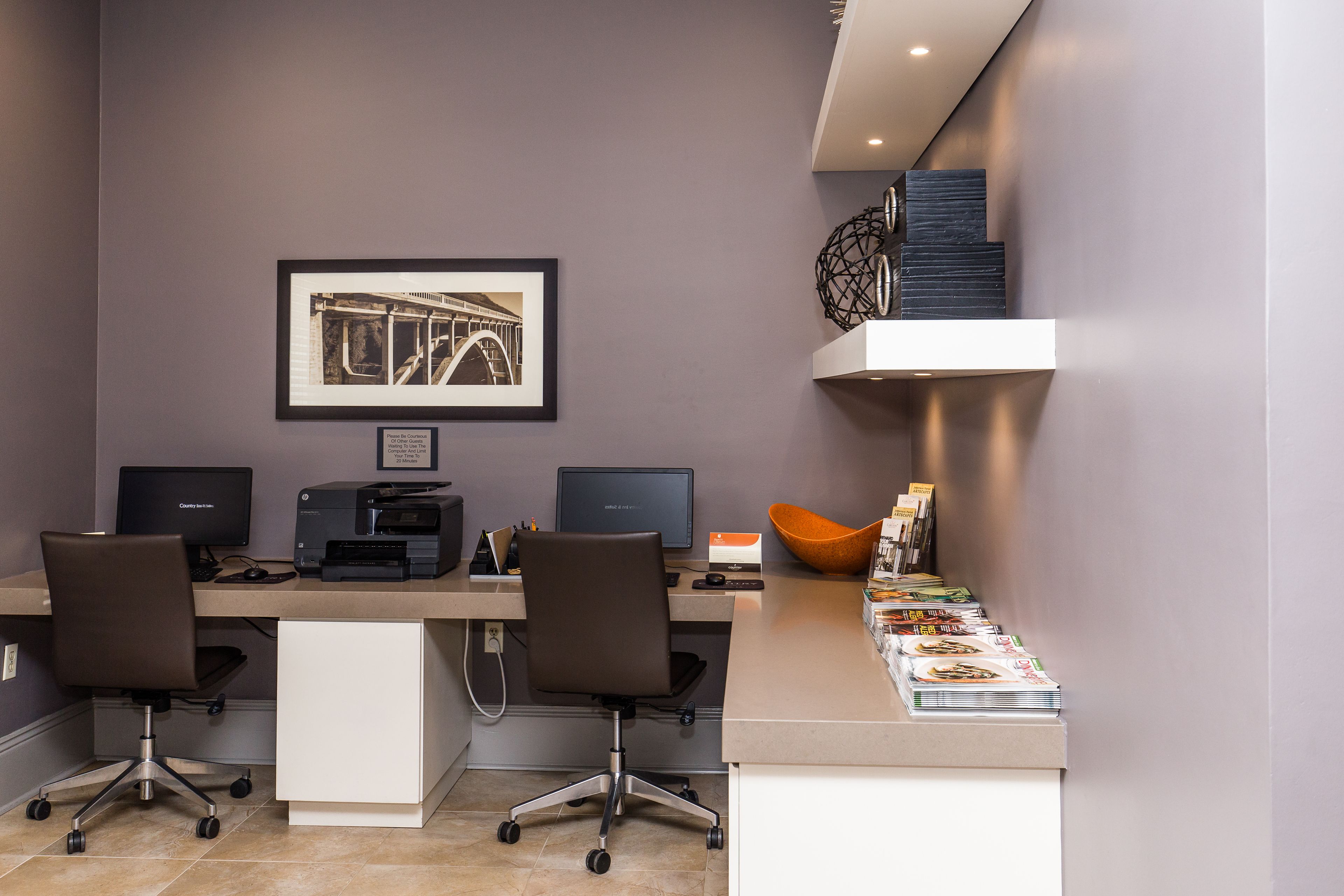 Un bureau moderne avec deux bureaux, des chaises, des ordinateurs et un tableau encadré accroché au mur.