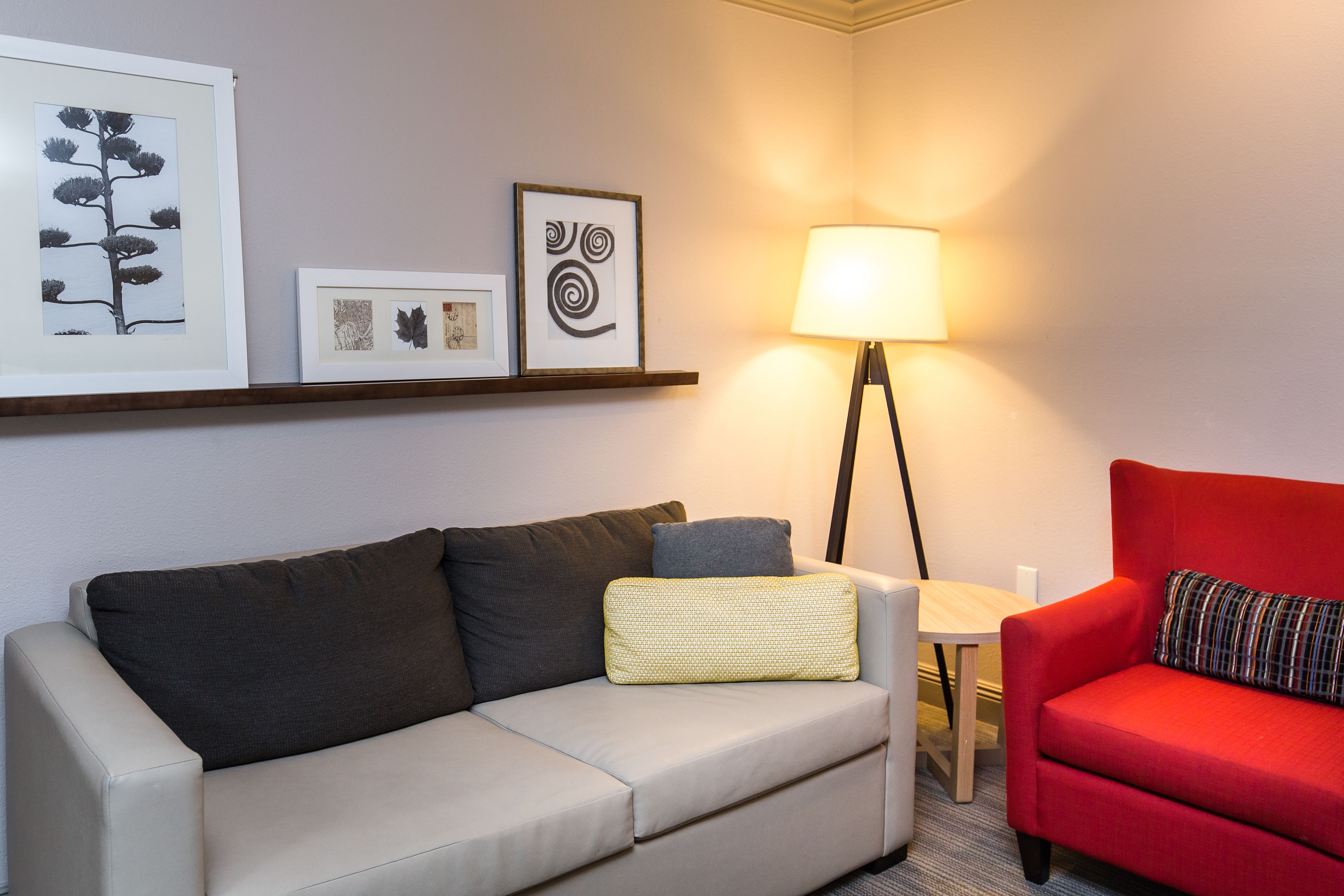 A modern living room with a beige sofa, a red armchair, a floor lamp, and framed artwork on the wall.