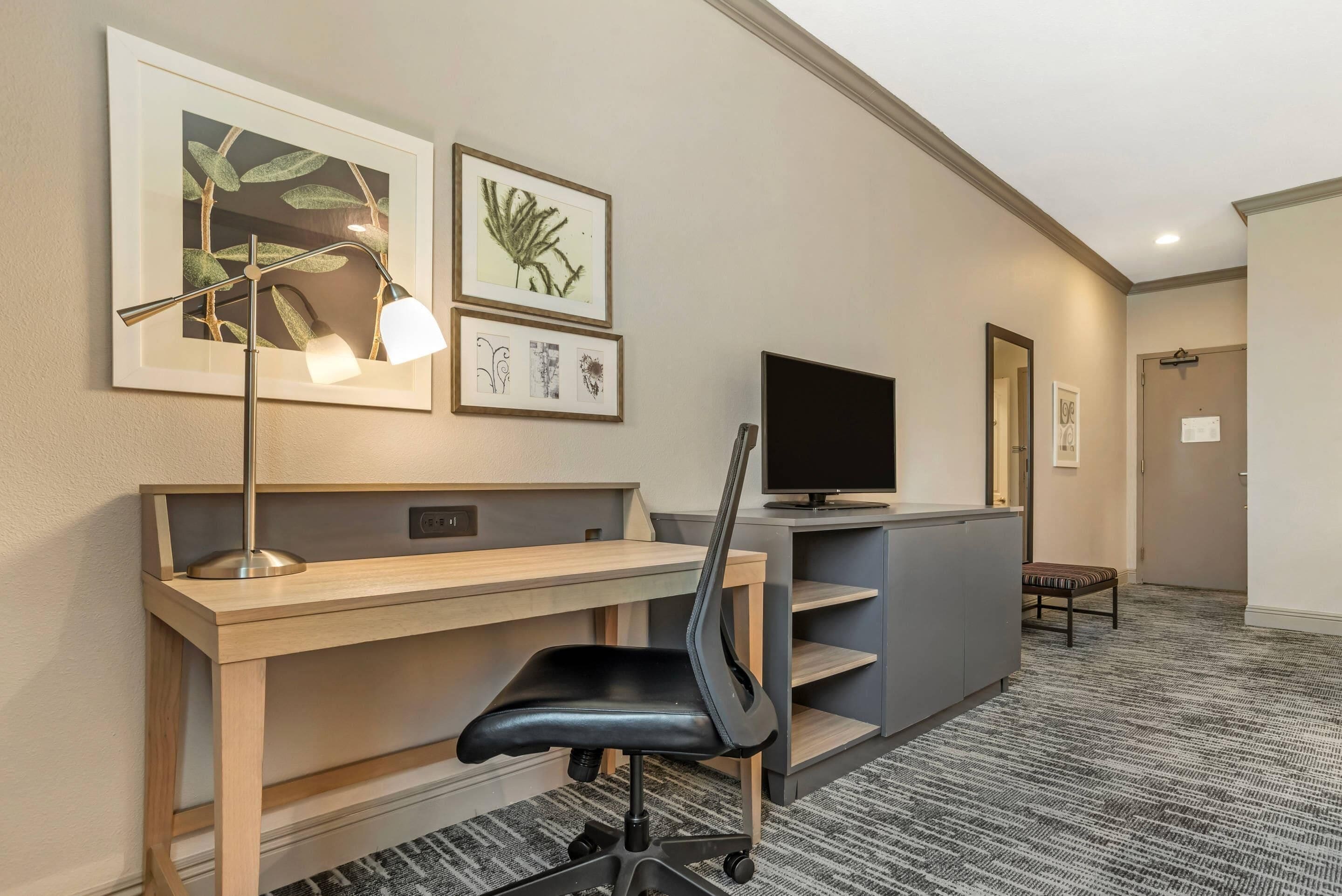 Une chambre d’hôtel équipée d’un bureau, d’une chaise, d’une télévision, d’œuvres d’art et dotée d’un sol recouvert de moquette.