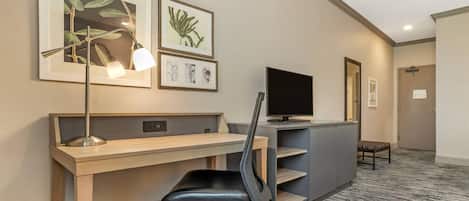Une chambre d’hôtel équipée d’un bureau, d’une chaise, d’une télévision, d’œuvres d’art et dotée d’un sol recouvert de moquette.