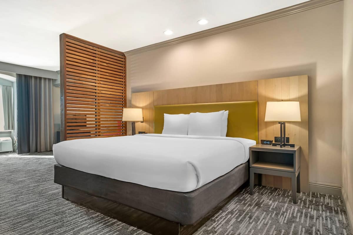 A hotel room with a large bed, two bedside tables, a wooden headboard, and a carpeted floor.
