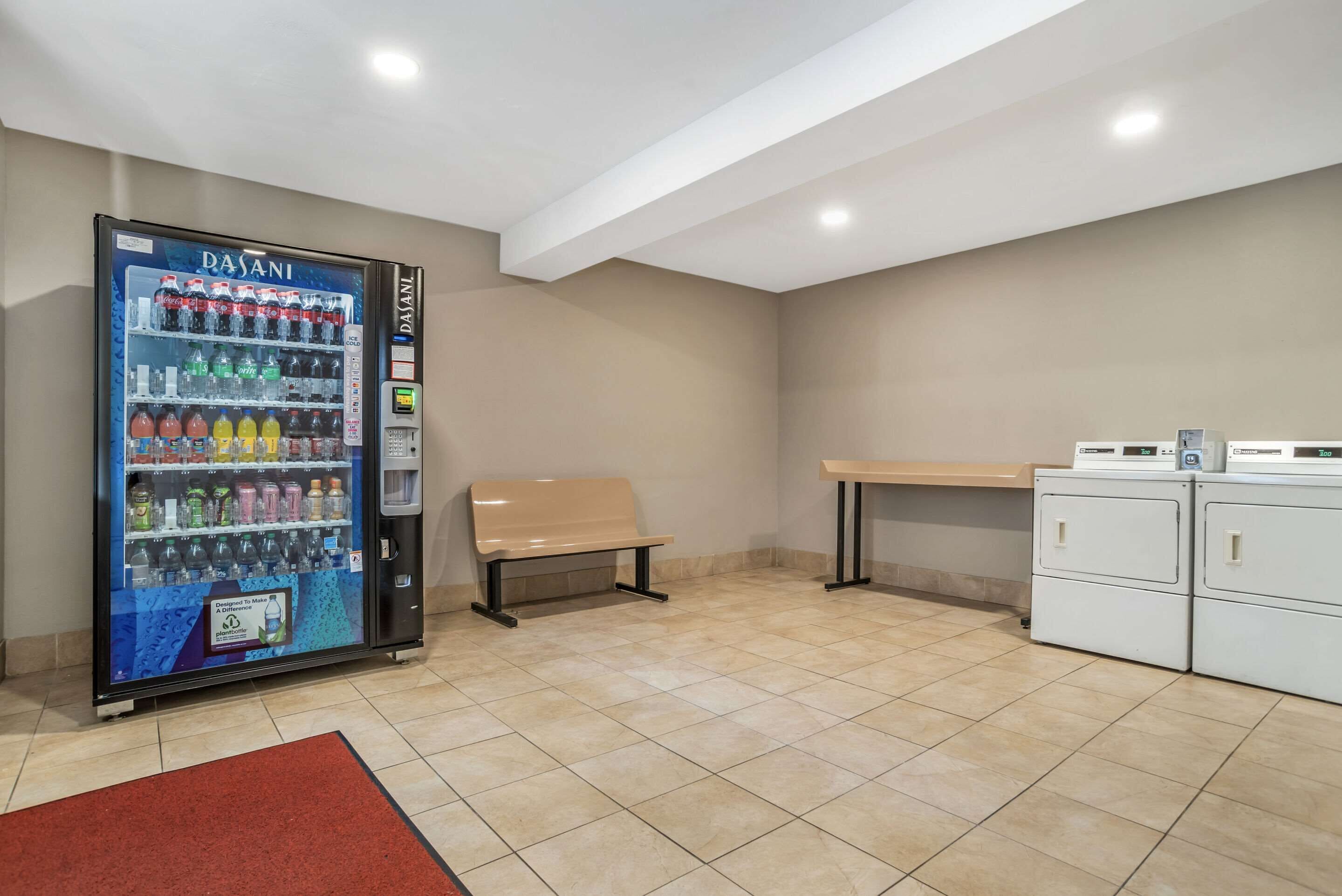 A vending machine with various drinks, a bench, a table, and a laundry area.