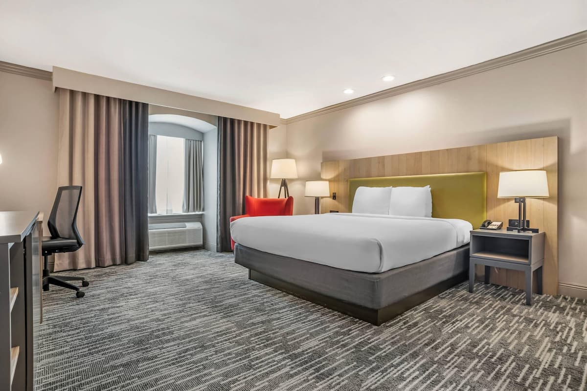 A hotel room with a bed, desk, chair, lamps, and a view of the outdoors.