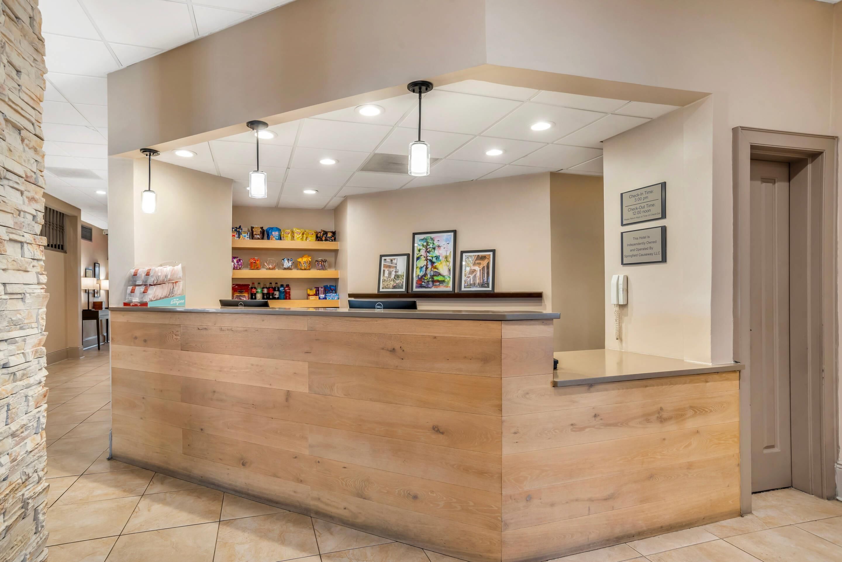 A reception desk with a wooden finish, overhead lighting, and framed pictures on the wall.