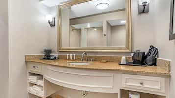 Un bagno con uno specchio grande, un lavandino, una macchina del caffè, asciugamani e un cestino.