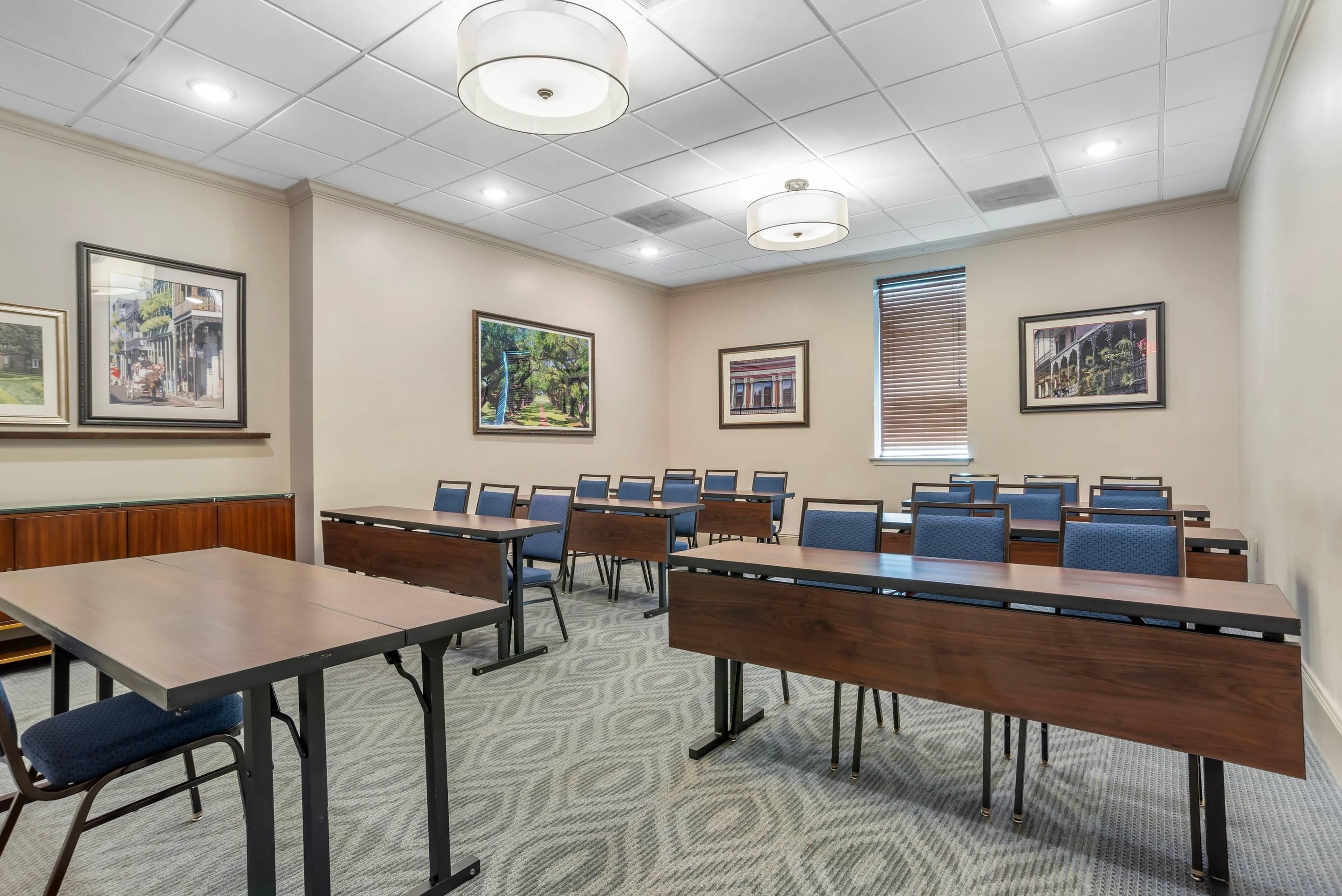 A conference room with multiple tables and chairs, framed pictures on the walls, and a carpeted floor.