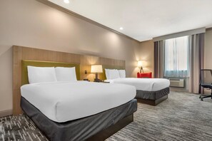 Een hotelkamer met twee bedden, een bureau, een stoel, een lamp en een groot raam.