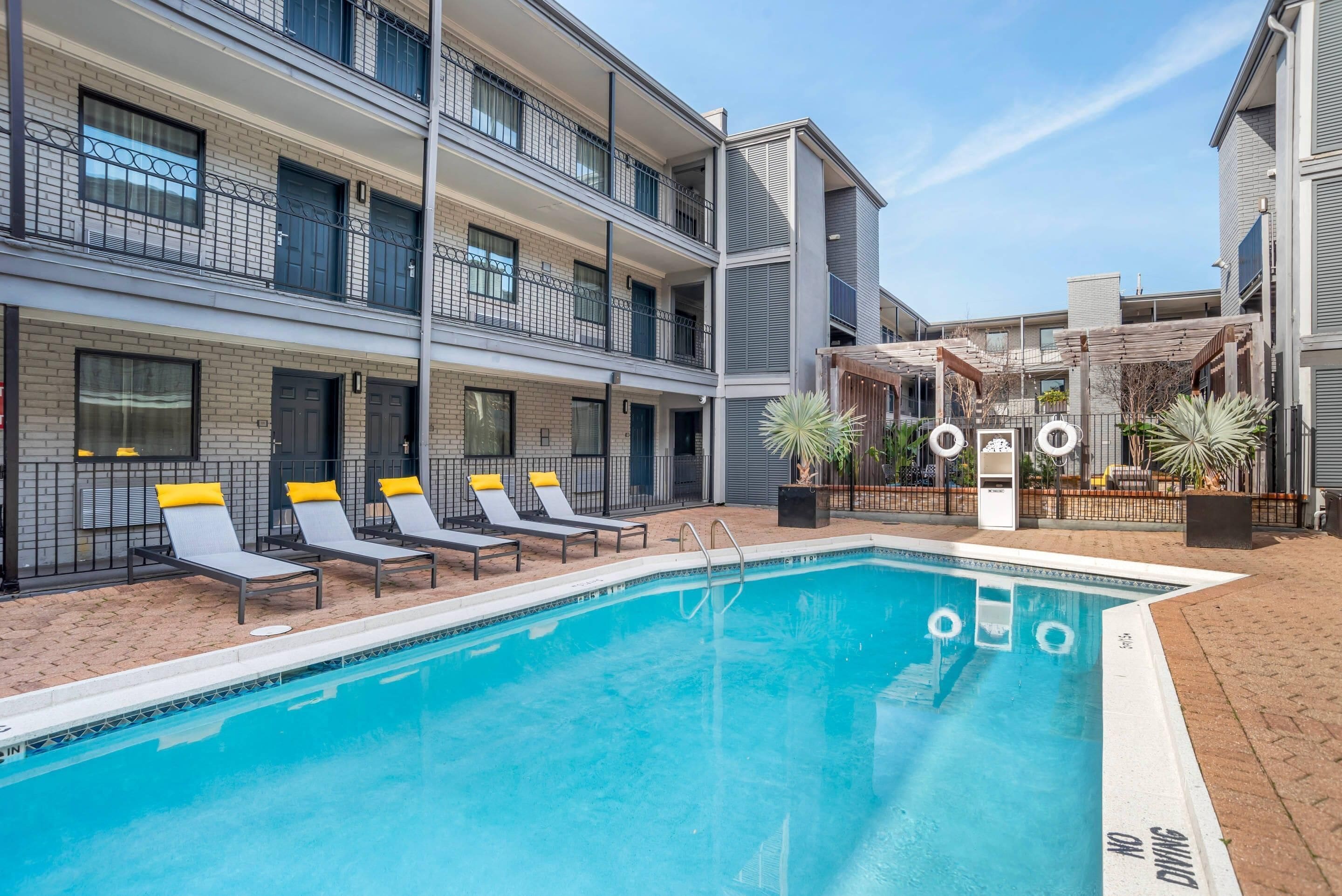 Un hotel de varios pisos con piscina, tumbonas y un área exterior techada.