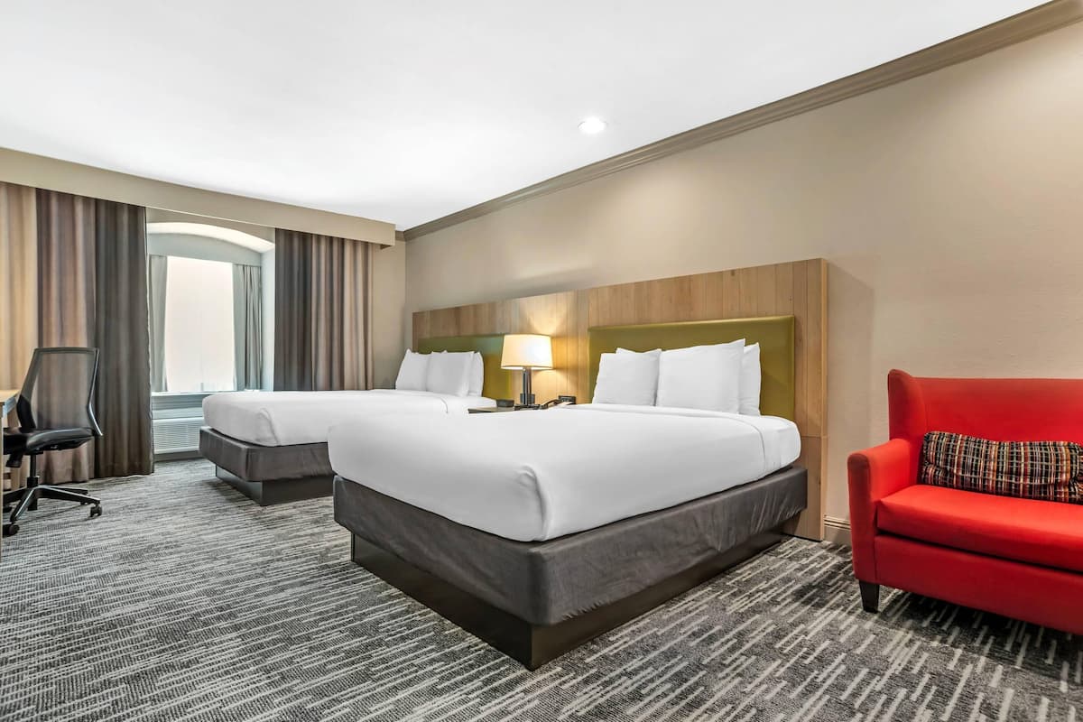 A hotel room with two beds, a desk, a chair, and a red sofa.