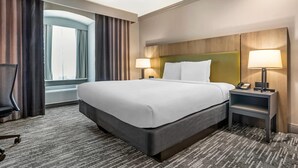 Ett hotellrum med en stor säng, två sänglampor, en telefon, en stol och utsikt över omgivningarna.