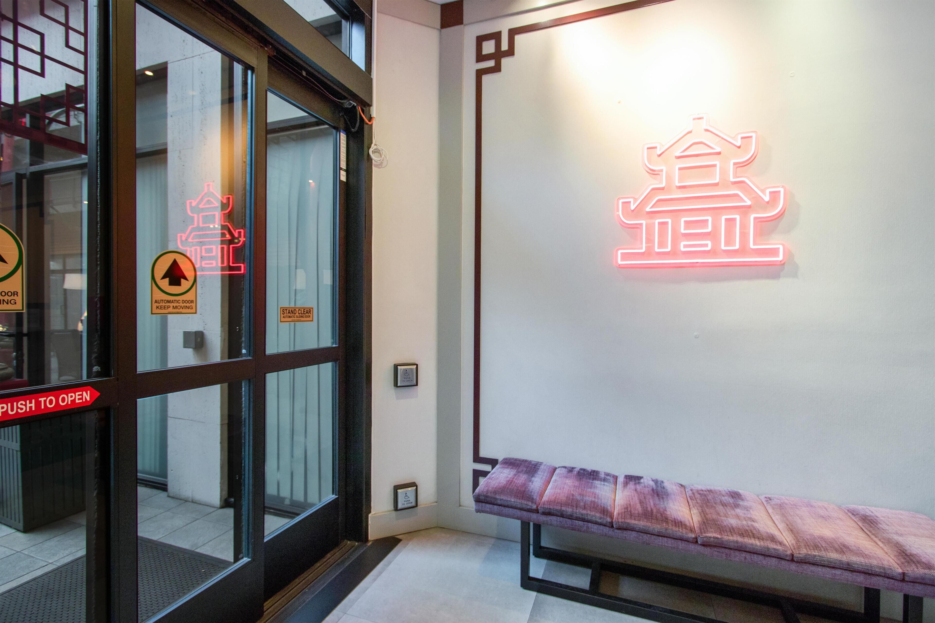 A hotel entrance with automatic doors, a bench, and a neon sign on the wall.