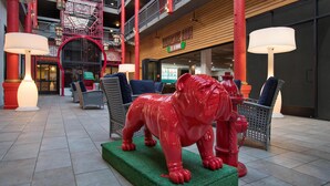 A spacious indoor area with a red fire hydrant sculpture, wicker furniture, and a staircase. - Aiden Los Angeles Downtown Dragon Gate Inn (Los Angeles)