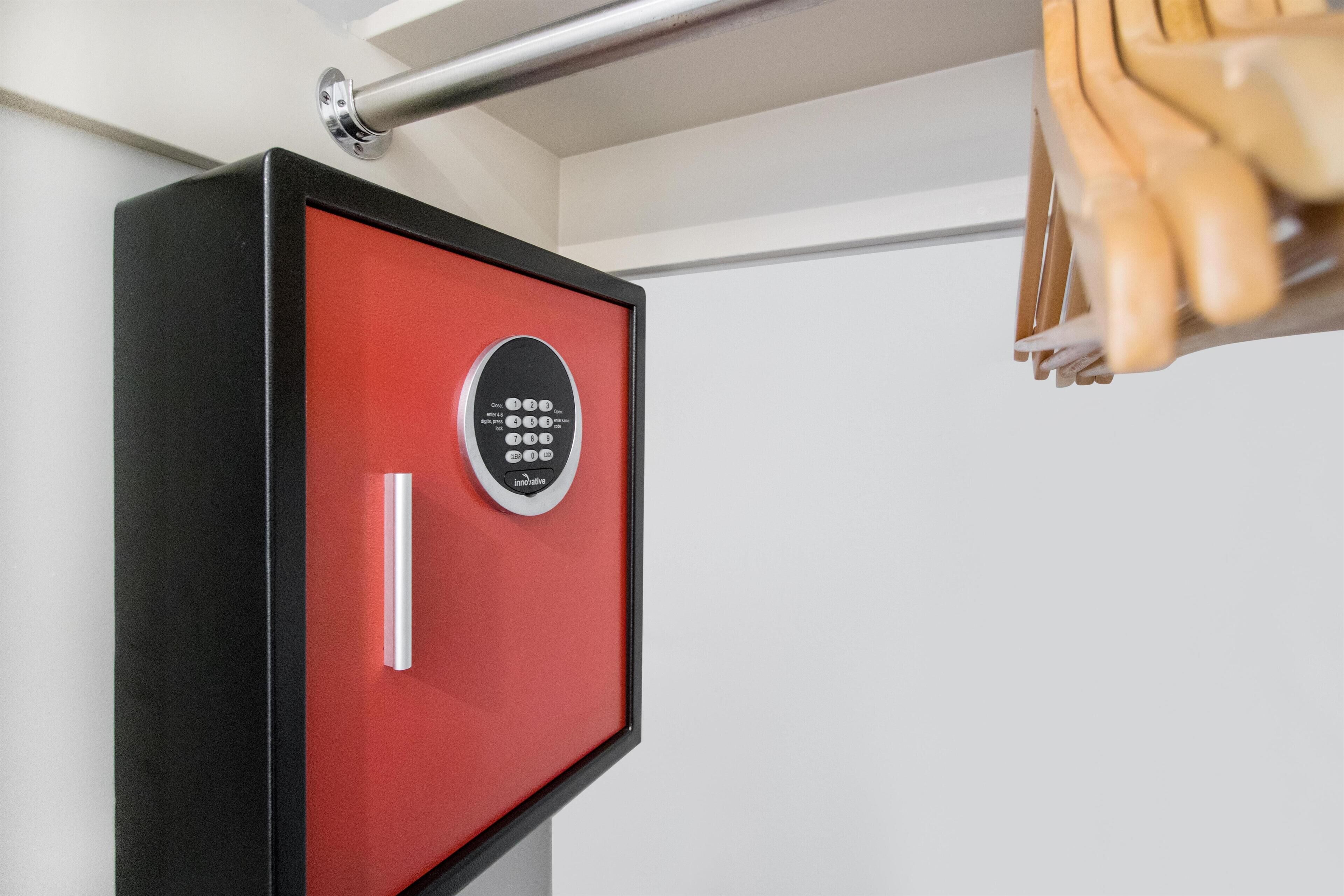 A red safe with a keypad lock mounted on a white wall.