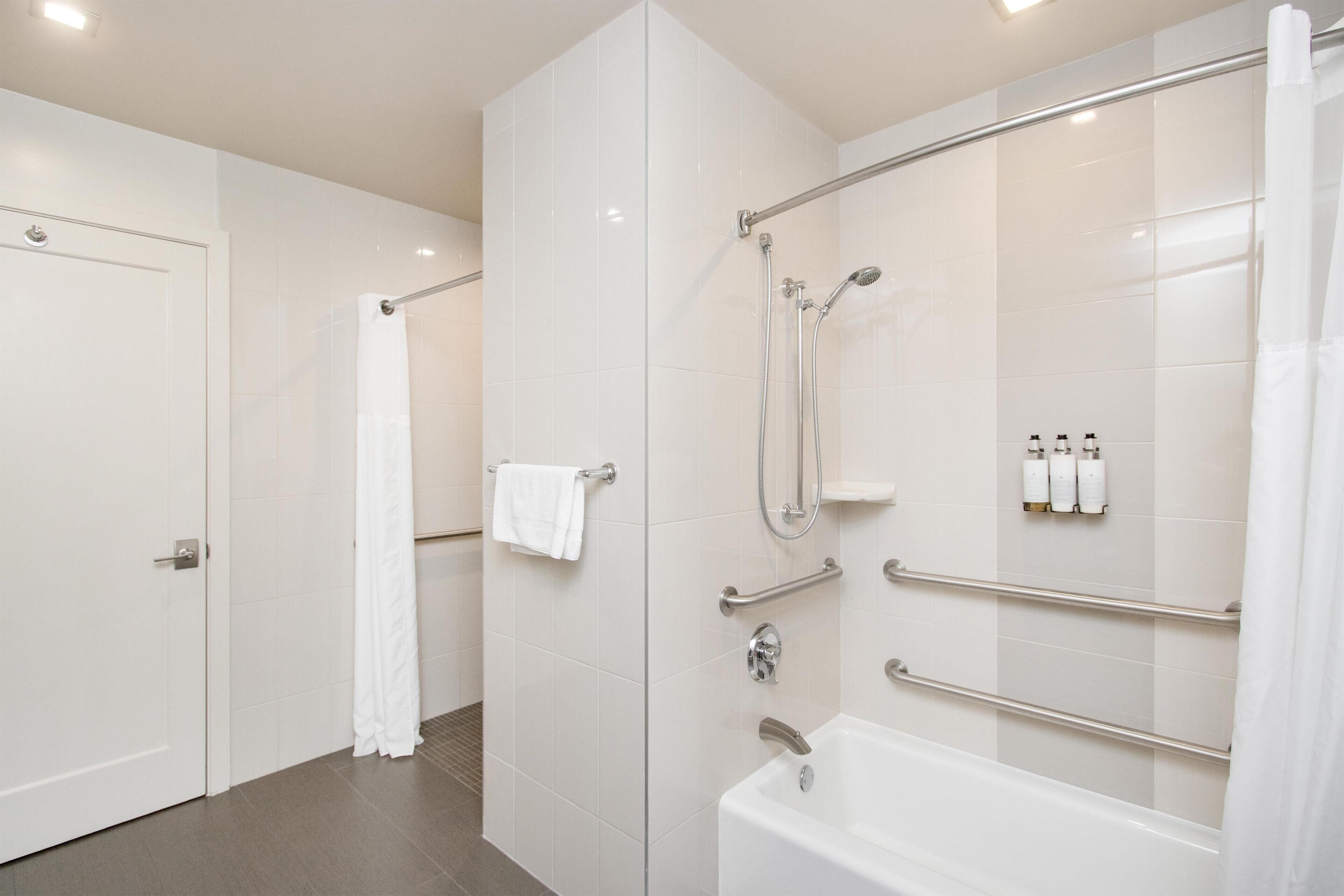 A modern bathroom with a bathtub, shower, and handrails.