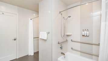 A modern bathroom with a bathtub, shower, and handrails.