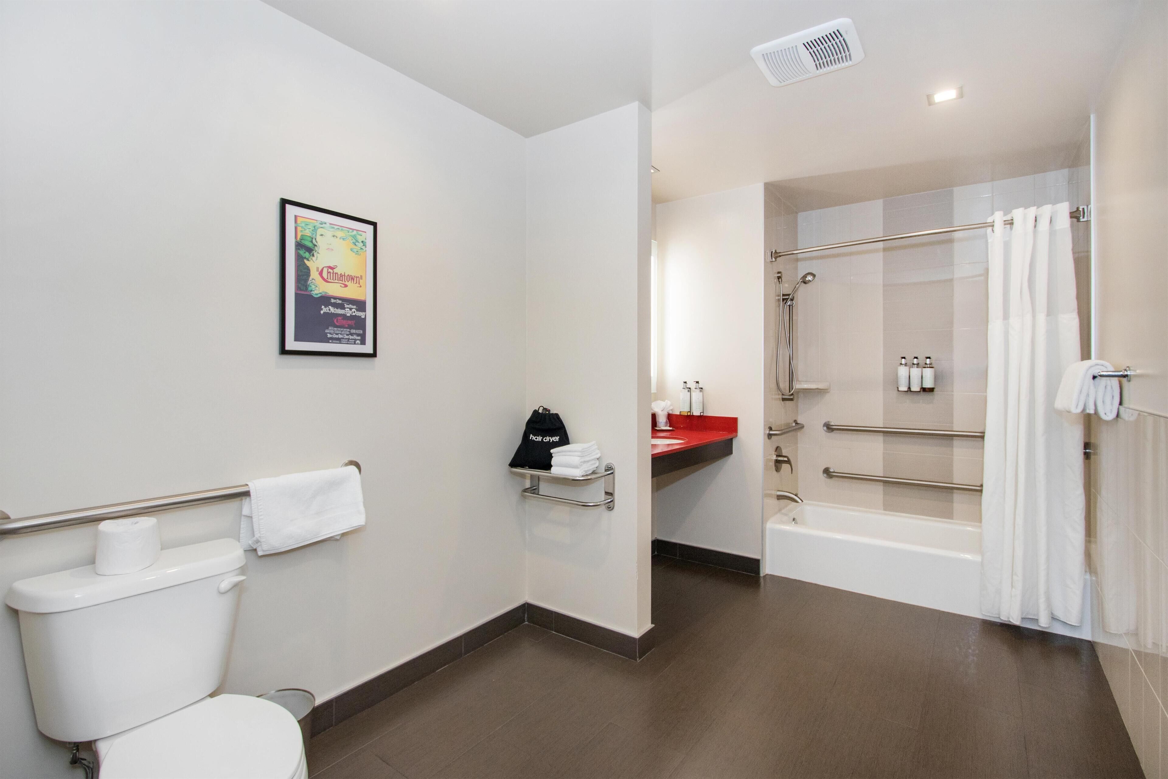 Une salle de bain moderne équipée de toilettes, d’une affiche encadrée, d’un sèche-cheveux, d’une douche et d’un lavabo rouge.