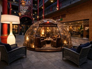 Une salle à la lanterne rouge, dotée d’un dôme de verre, aménagée avec des fauteuils en cuir et une table centrale, entourée de chaises en osier.