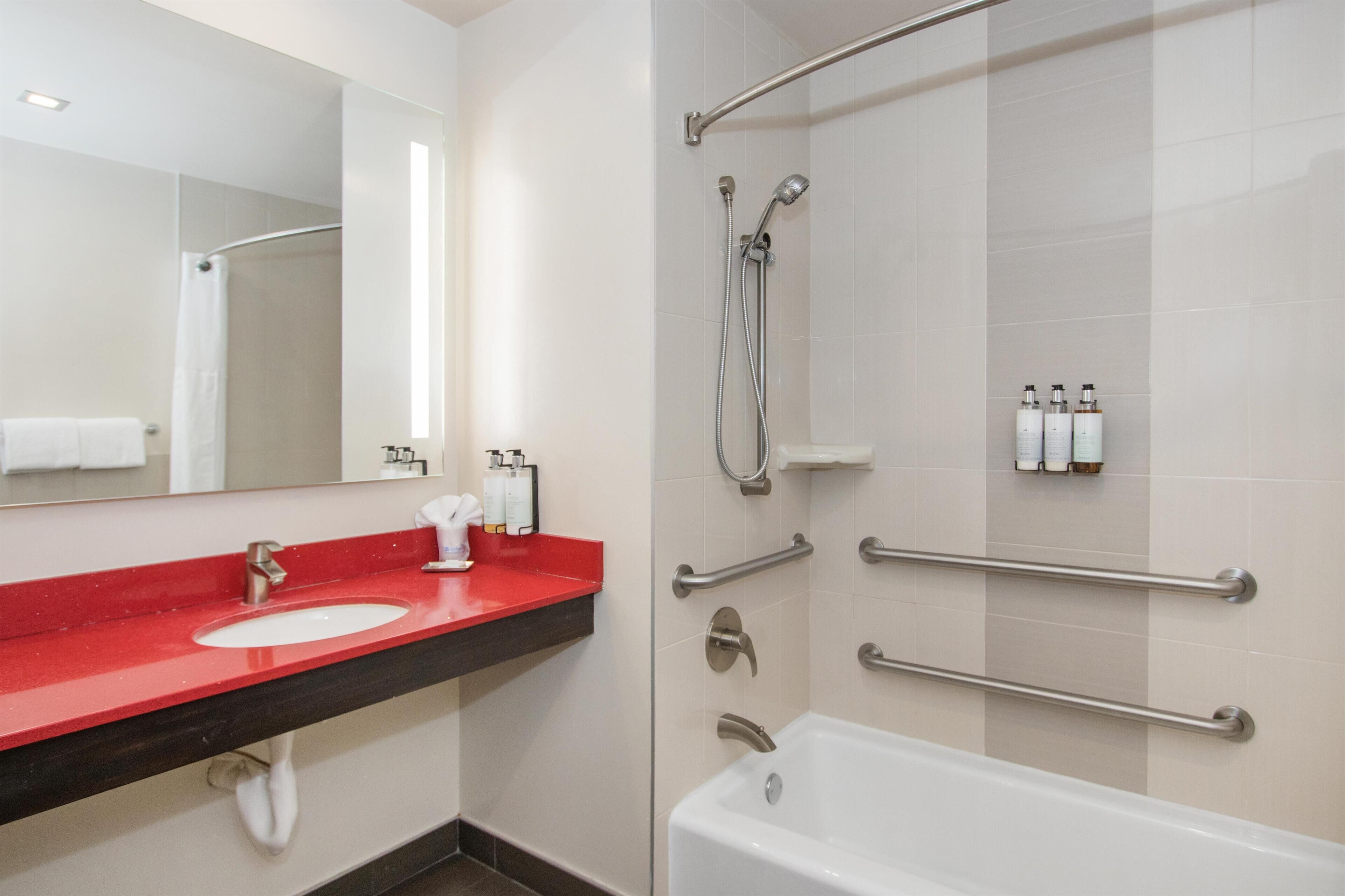 A modern bathroom with a red sink, a white bathtub, and a shower area.