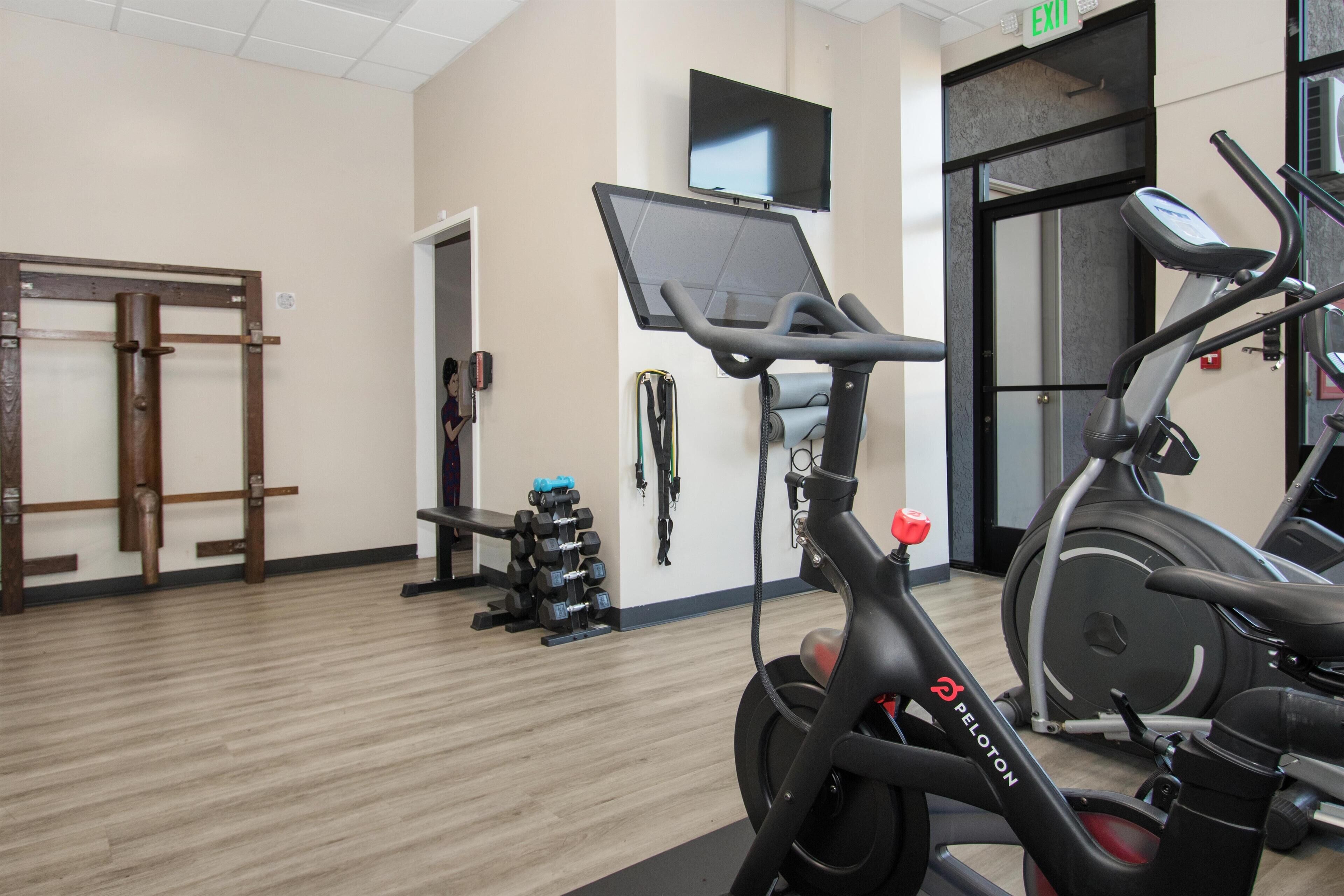 Un gimnasio con equipo de ejercicio, un televisor en la pared y una señal de salida.