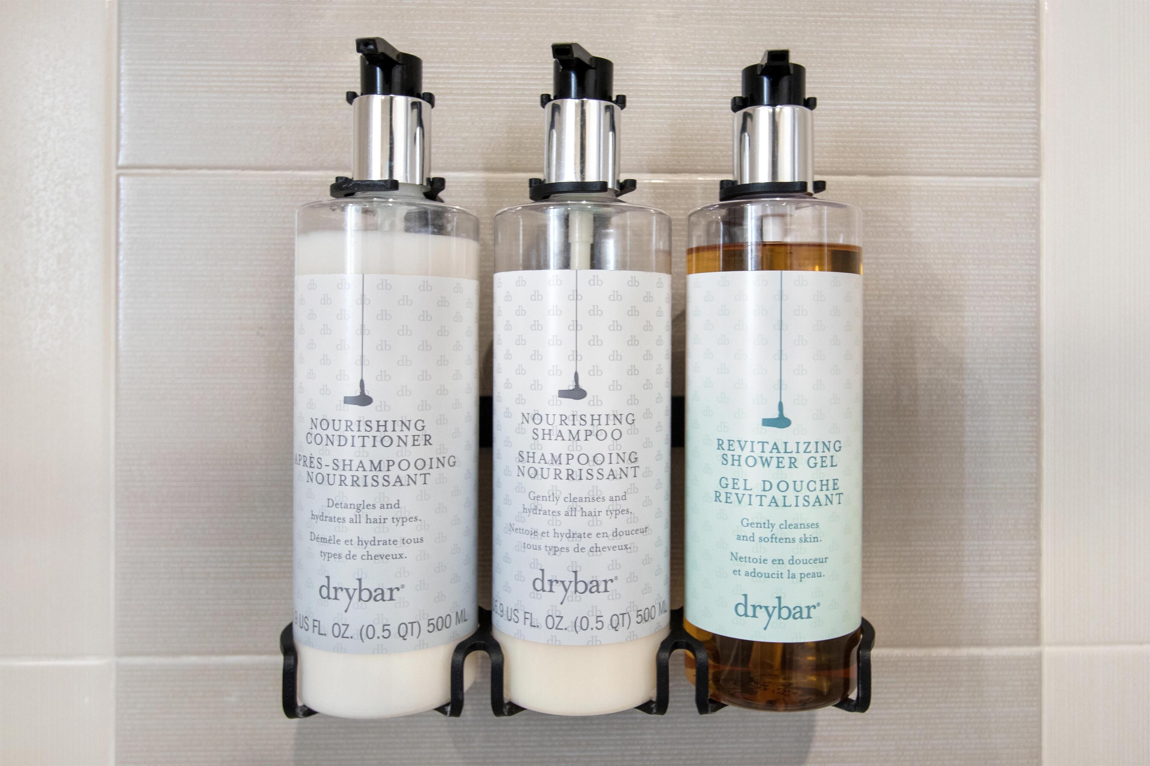 Three bottles of drybar products on a tiled wall.