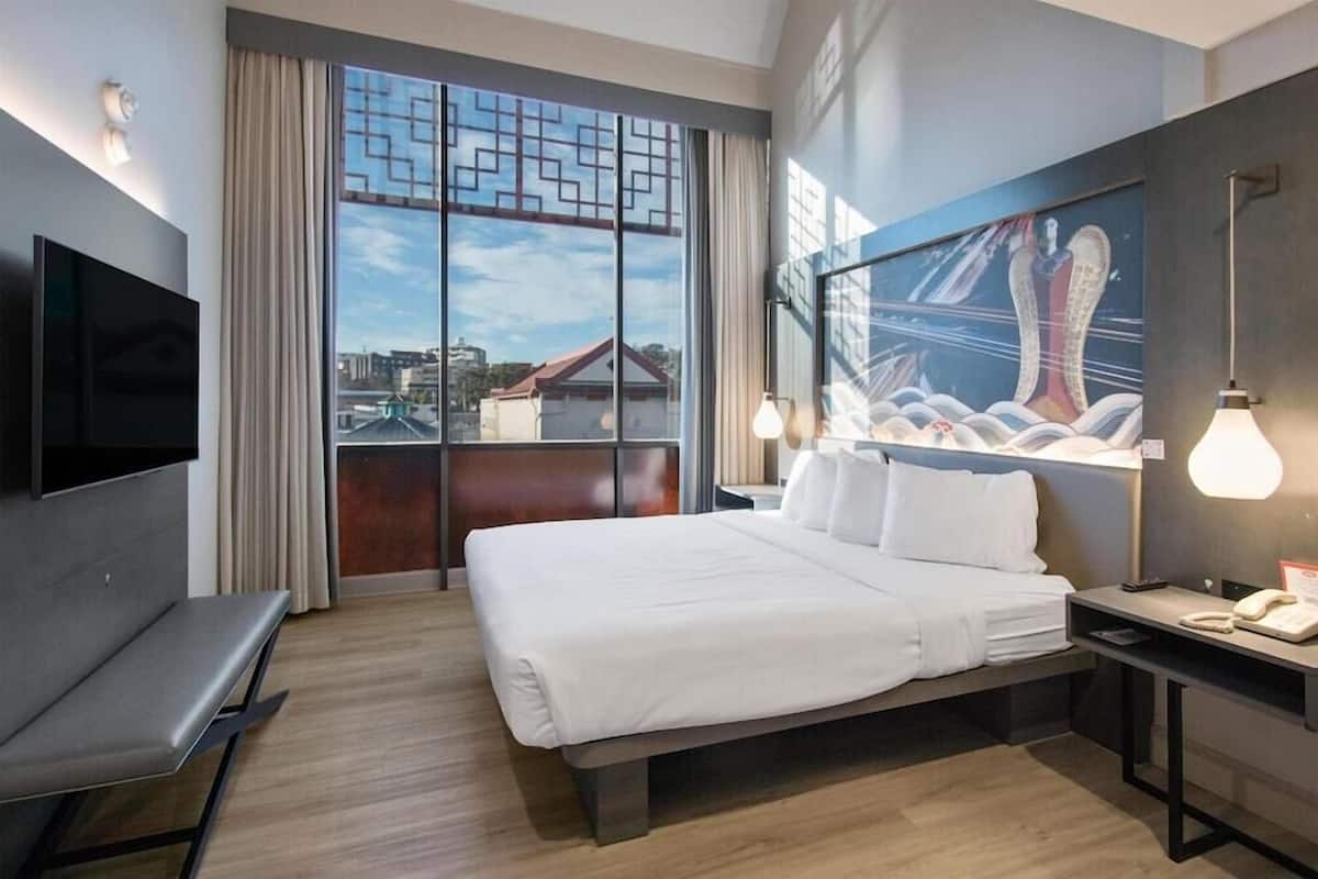 A hotel room with a large bed, a TV, a desk, a chair, and a painting on the wall.