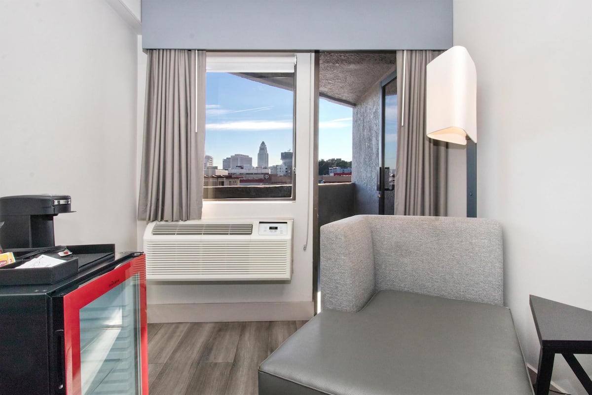 A modern hotel room with a city view, a sofa, a small table, and an air conditioning unit.
