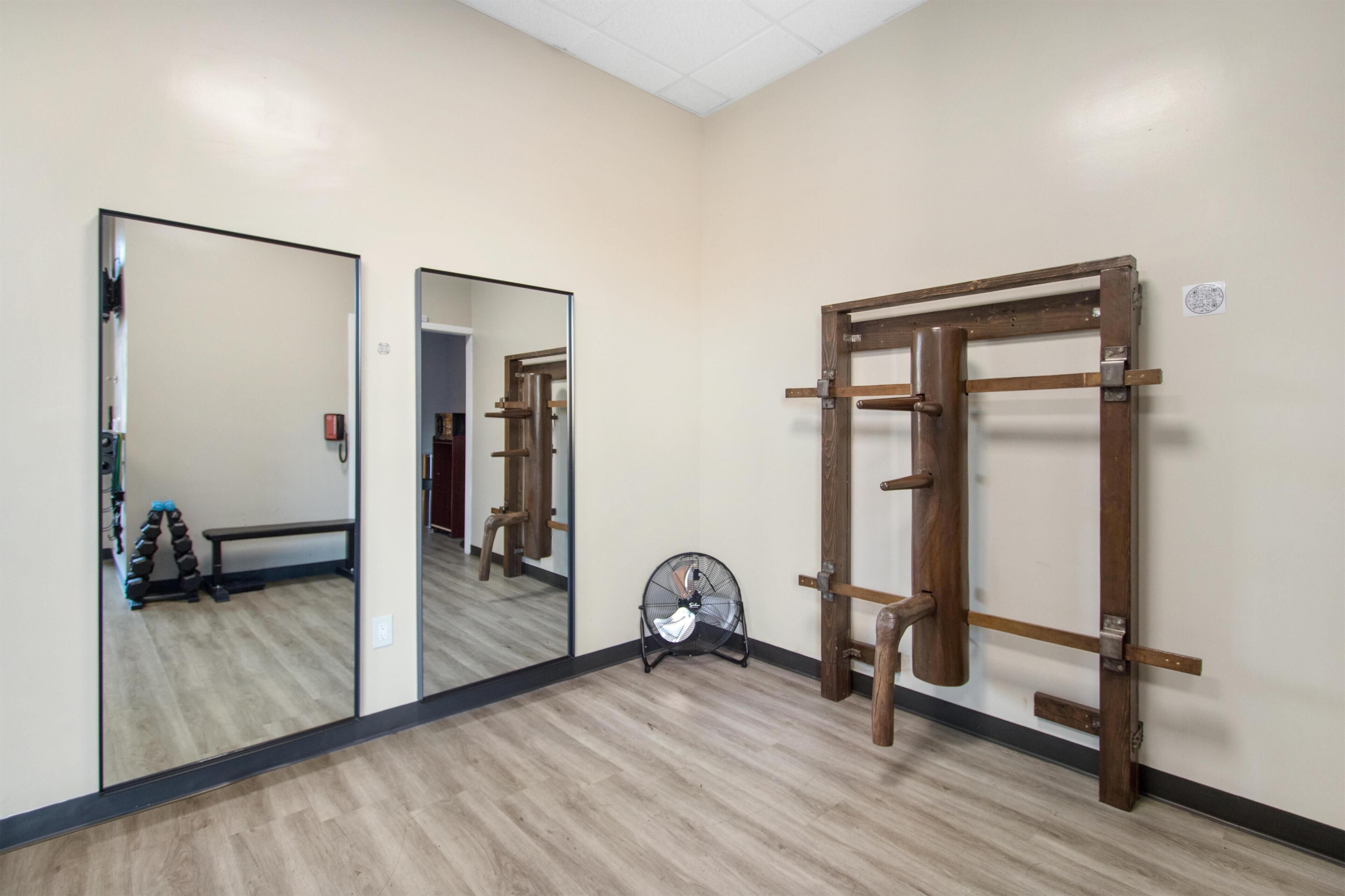 Una habitación con un perchero de madera, un ventilador y un banco con mancuernas.