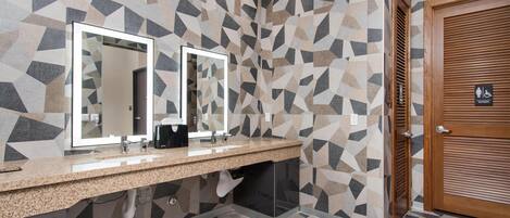 A modern bathroom with geometric patterned walls, a granite countertop, dual mirrors, and a wooden door with a women's restroom sign.