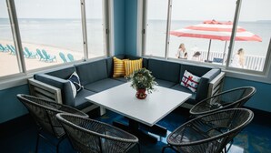 A room with a large window overlooking the beach, a white table, and wicker chairs. - Breakers Resort & Beach Bar (St Ignace)