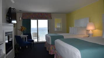 A hotel room with two beds, a desk with a chair, a TV, and a view of the ocean.