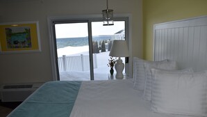A hotel room with a large bed, a view of the sea through a sliding door, a white radiator, and a framed picture on the wall. - Breakers Resort & Beach Bar (St Ignace)