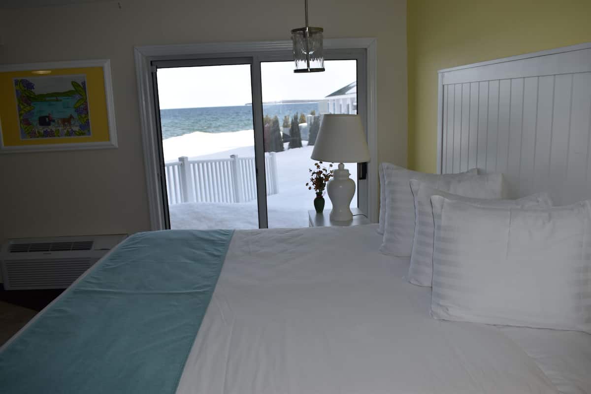 Ein Hotelzimmer mit einem großen Bett, Blick auf das Meer durch eine Schiebetür, einem weißen Heizkörper und einem gerahmten Bild an der Wand.