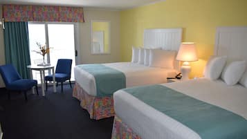 A hotel room with two beds, a small table with chairs, a lamp, and a view of the outside.