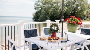 A white table set outdoors with a view of the sea, surrounded by white chairs and a pink umbrella. - Breakers Resort & Beach Bar (St Ignace)