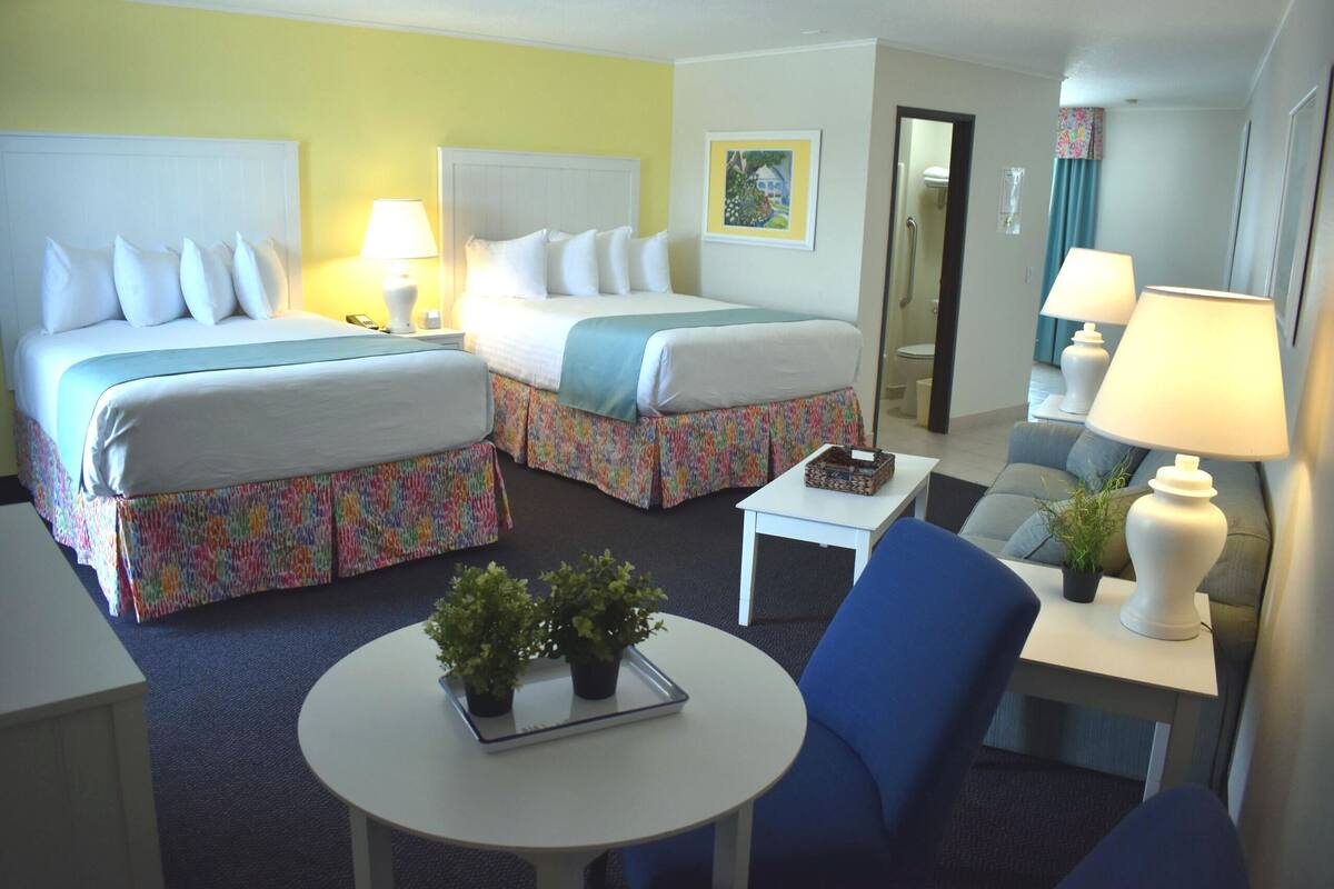 Ein Hotelzimmer mit zwei Betten, einem kleinen Tisch mit Pflanze, einem Sessel und einer Lampe.