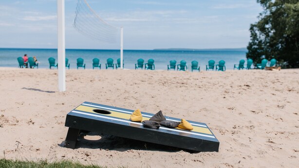 A beach volleyball net with chairs and cushions in the sand.