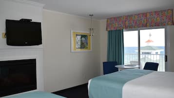 A hotel room with two beds, a TV, a fireplace, a painting, a balcony with a view of the sea, and a table with chairs.