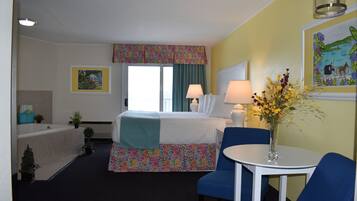 A hotel room with a bed, a small table with a vase, a chair, a window with curtains, a wall-mounted lamp, and a painting.