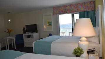A hotel room with a bed, a desk with a television, a lamp, and a view of the sea.