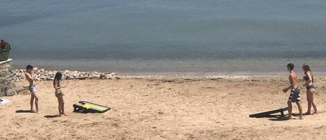 A sandy beach with a few people standing and a surfboard.