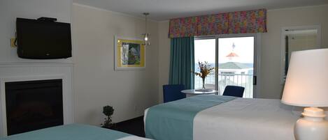 A hotel room with two beds, a television, a fireplace, a dining table with chairs, and a window with a view.