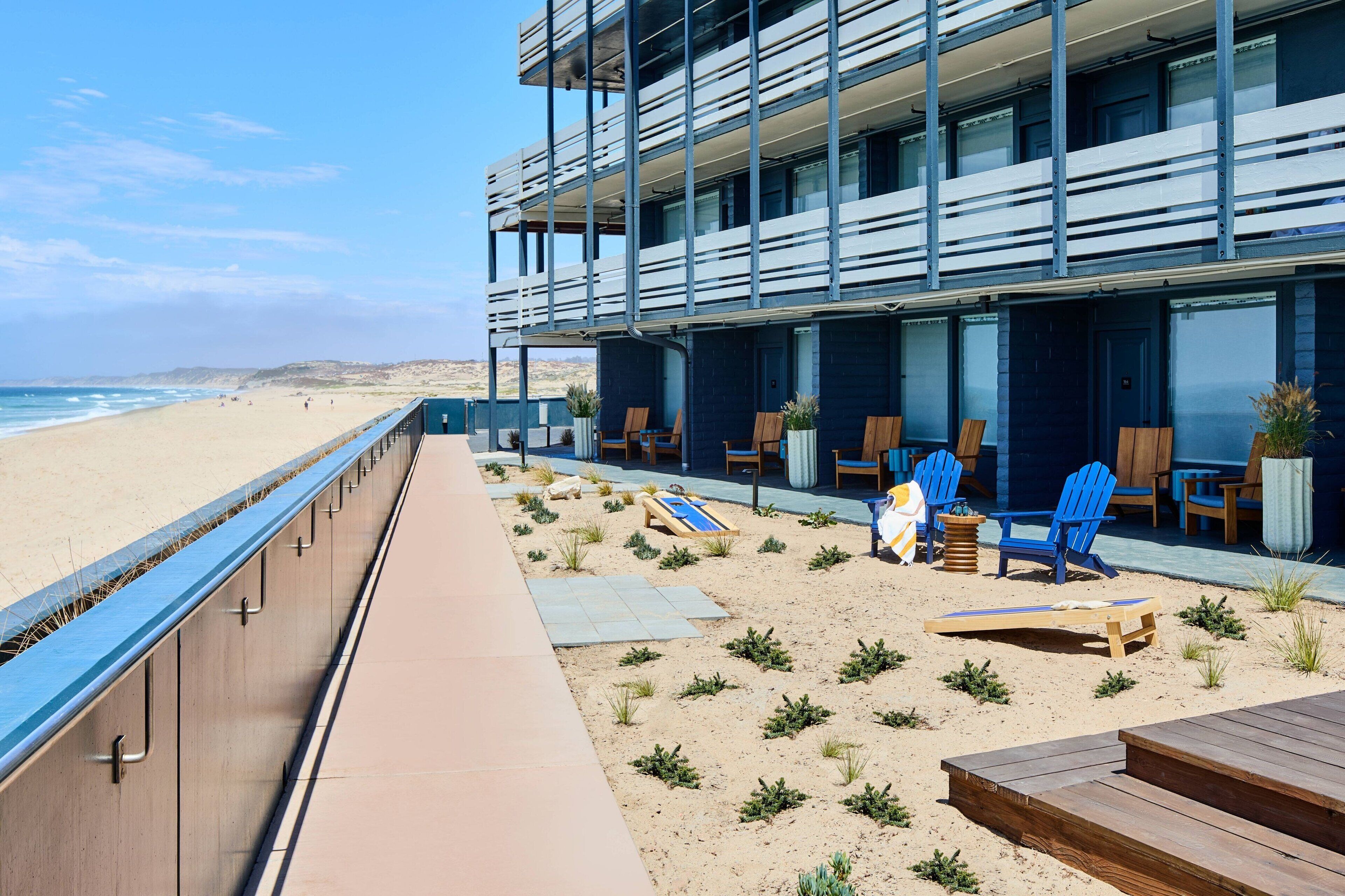 A beachfront hotel with a balcony overlooking the beach, lounge chairs, and a small garden area.